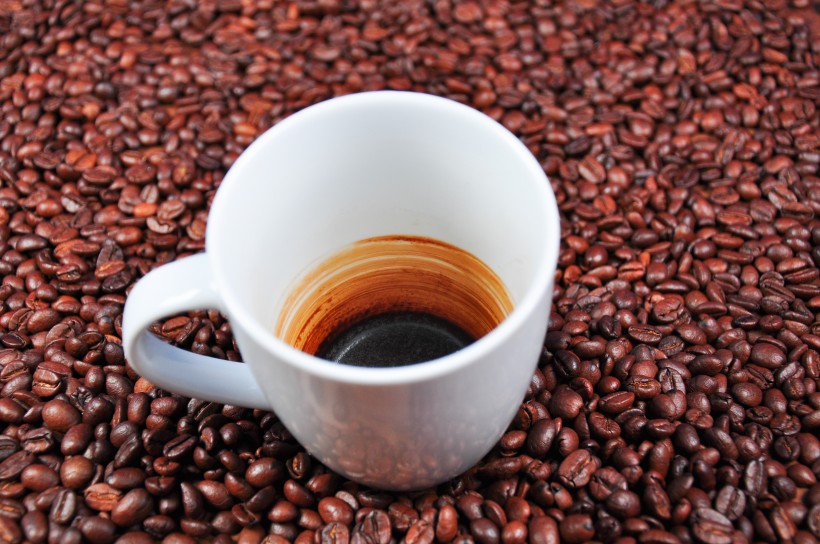 咖啡豆散落在装有咖啡的杯子旁图片