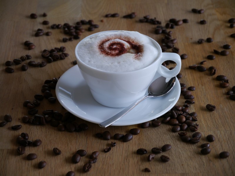 咖啡豆散落在装有咖啡的杯子旁图片